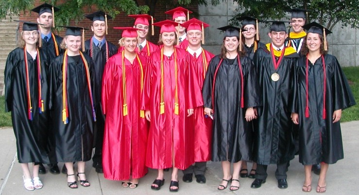 A group of people in red and black graduation gowns stand on a sidewalk.
